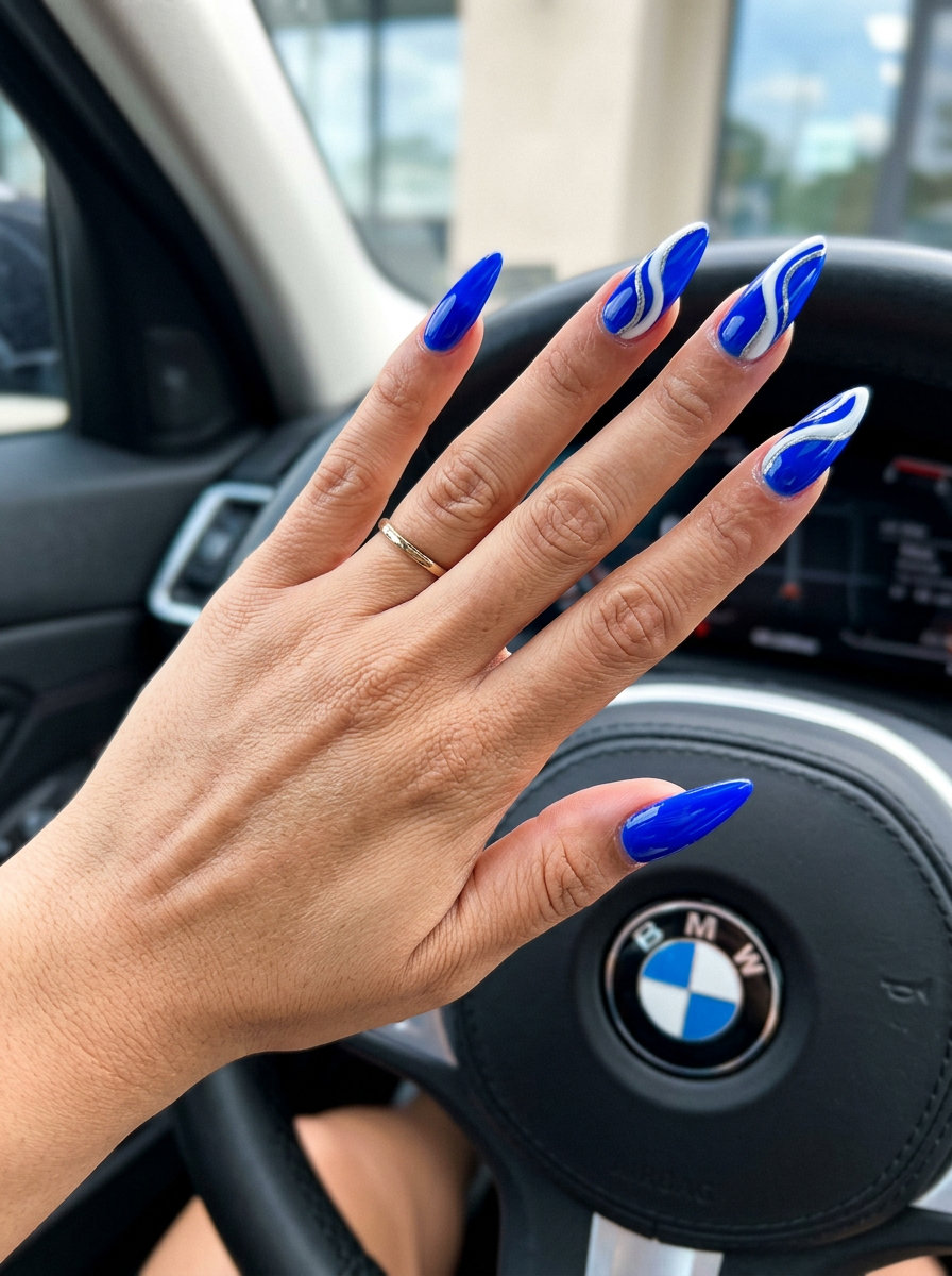 Electric cobalt blue stiletto nails with abstract white and silver swirls for an edgy party look. Blue summer nails 2026.