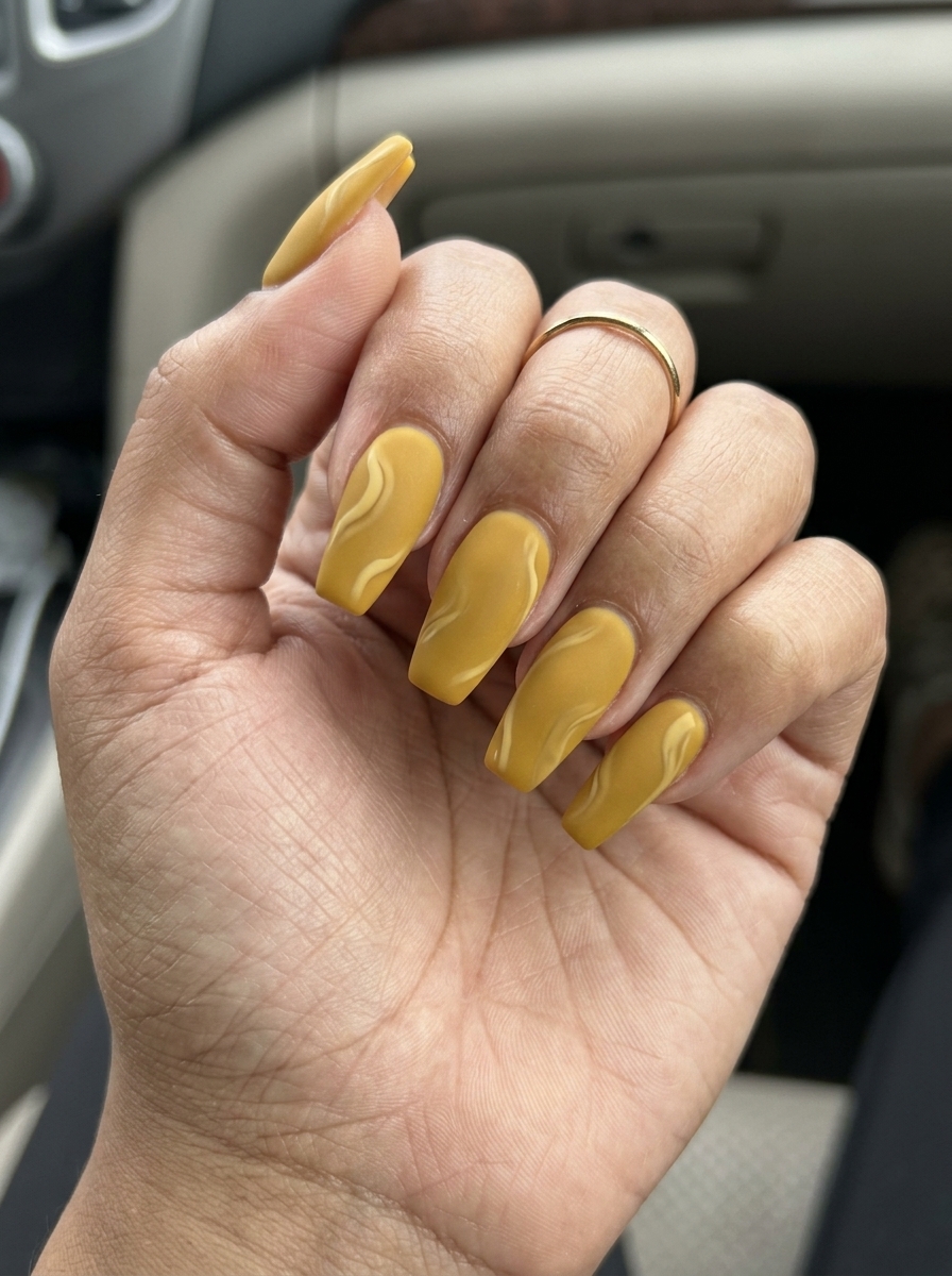 Yellow summer nails 2026: Sophisticated mustard yellow with cream swirls and velvet matte finish on coffin nails.
